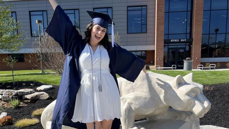 New Penn State graduate Anna Raffeinner celebrates with a joyful expression with the Lion Shrine on the Penn State DuBois campus, 就在PAW中心外面